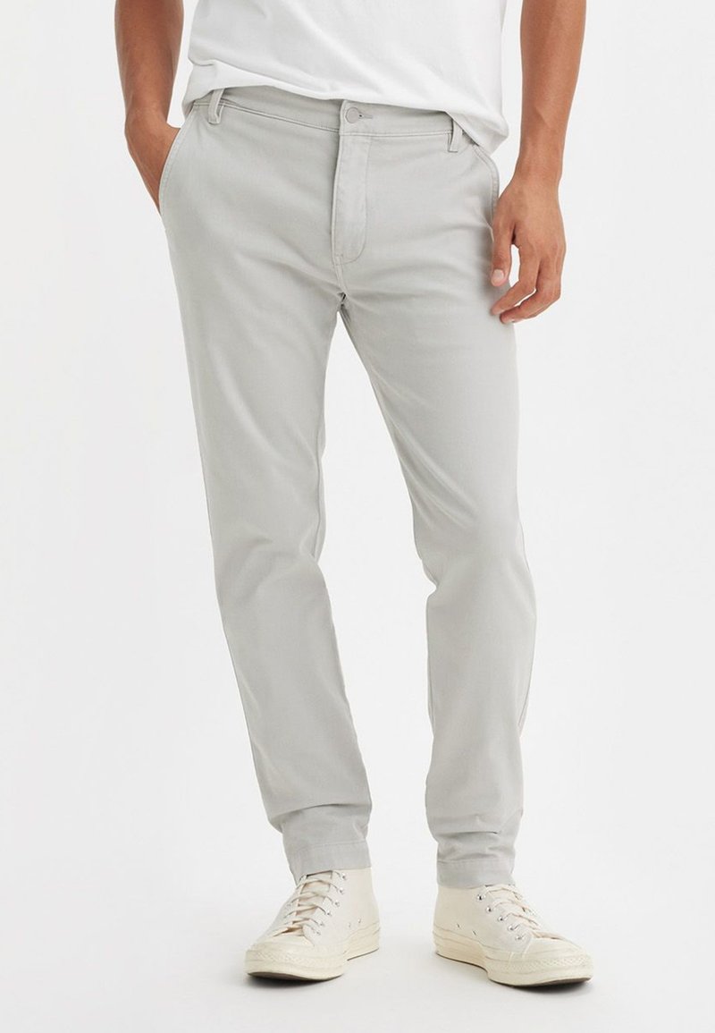 Chinos en coton gris clair à coupe slim, avec poches avant et fermeture à glissière. Assortis à des baskets montantes blanches pour le contraste.