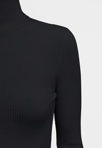Schwarzer, gerippter Rollkragenpullover mit taillierter Passform und glatter Textur. Der Stoff hat vertikale Linien und einen hohen Kragen.
