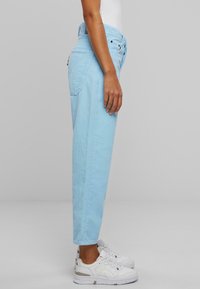 Pantaloni in corduroy azzurro chiaro con una vestibilità rilassata, dotati di un elastico in vita con cordoncino, tasche laterali e indossati con sneaker bianche.