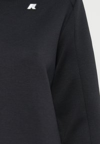 Sweatshirt noir avec une texture douce, présentant un logo subtil sur le haut à gauche. Le design comprend des manches longues et un col rond.
