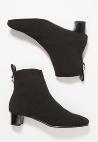 Bottines noires avec une tige tricotée façon chaussette, un bout pointu et un petit talon bloc. Elles comportent un détail zippé à l'arrière.