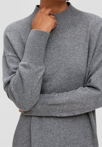 Maglione grigio lavorato a maglia con colletto alto a coste, spalle cadute e polsini a coste. Texture morbida e vestibilità rilassata. Design minimalista.