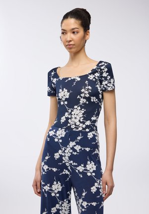 Tuta floreale blu navy con maniche corte, scollo quadrato, stampa floreale bianca, tessuto con una texture morbida e corpetto aderente che si trasforma in gambe morbide.