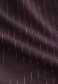 Tissu bordeaux à la texture lisse, présentant de fines rayures blanches verticales. Le matériau semble léger et subtilement orné de motifs.