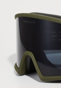 Ski goggles med svart reflekterande lins, olivgrön gummiram och svart skumvaddering. Har "Oakley"-logotypen på sidan.
