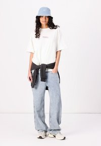 Hvit oversized t-skjorte, lyseblå bøttehatt, svart sweatshirt knyttet rundt livet, lyseblå baggy jeans, hvite og beige sneakers.