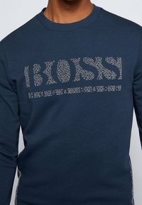 Maglietta a maniche lunghe blu navy in tessuto morbido con un motivo logo testurizzato realizzato con piccoli borchiette lucide sulla parte anteriore.