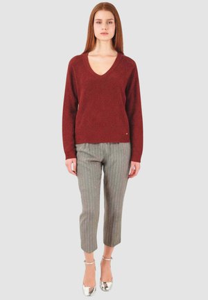 Maglione a V in maglia borgogna, pantaloni sartoriali grigi con righe sottili e scarpe con tacco argento su uno sfondo semplice e neutro.