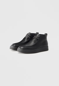 Une paire de bottines noires en cuir avec des lacets et une surface texturée sur fond blanc.