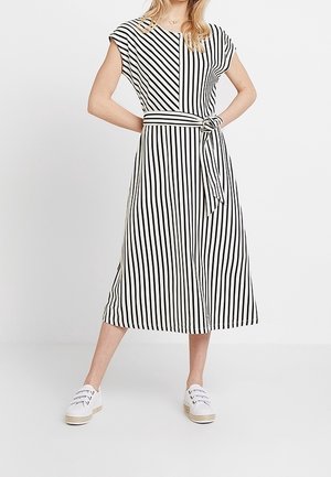 Mujer con un vestido midi de rayas verticales negras y blancas, con un cinturón atado en la cintura y zapatillas blancas casuales.