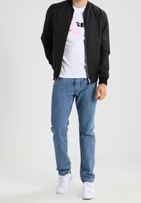 Black bomber jacket over a white T-shirt with a pink graphic, paired with blue jeans and white sneakers. Simple design with zip closure.