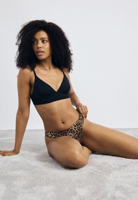 Black bralette with V-neckline and thin straps, paired with leopard print high-waisted bottoms, displayed on a soft, neutral background.
