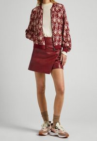 Bordeaux-gepatroneerde bomberjack, crèmekleurige top, kastanjebruine leren minirok en roze sneakers met tan accenten en crèmekleurige veters.