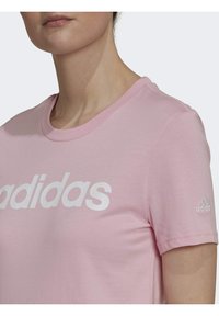 Růžové bavlněné tričko s bílým logem "adidas" přes hruď a malým logem na rukávu, s klasickým kulatým výstřihem.