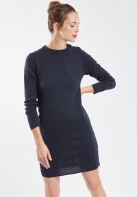 Navy blauwe gebreide jurk met lange mouwen, ronde hals en subtiele zijknopen. Slank gesneden ontwerp met een gladde textuur en een lengte tot halverwege de dij.