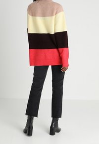 Pull surdimensionné multicolore à texture côtelée ; présente des rayures beige, crème, marron et corail vif. Associé à un jean noir et des talons.