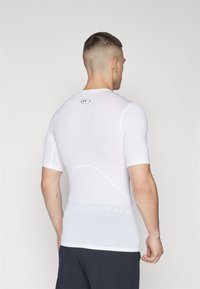 Hvid kortærmet træningsskjorte, tætsiddende design med struktureret stof, der har et logo i nakken og en diskret mærket talje.