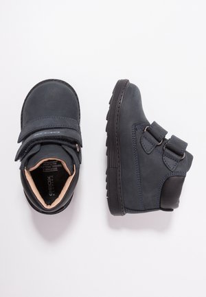 Ciemnoszare buty dla dzieci z regulowanymi podwójnymi paskami na rzep, wyściełanym kołnierzem i teksturowanymi gumowymi podeszwami, pokazane z góry i z boku.