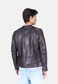 Giubbotto di pelle nera con una finitura leggermente invecchiata, caratterizzato da polsini con zip e un design del colletto semplice. Dettagli di cucitura visibili.