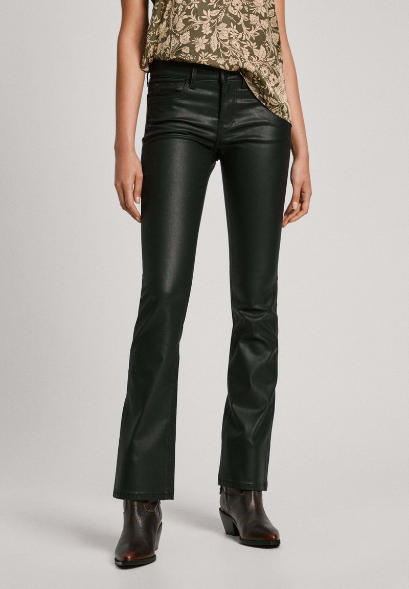 Femme portant un pantalon flare en cuir noir slim, des bottines marron et un top sans manches vert olive à motifs.