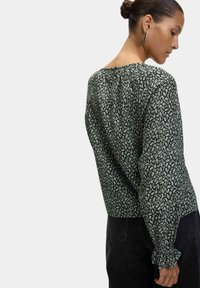 Black floral-patterned blouse with long sleeves, gathered neckline, and ruched cuffs, made from lightweight fabric with a soft texture.