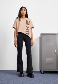 Világos bézs rövidujjú póló nagy fekete "NIKE" felirattal, fekete harangszárú leggings-szel és tömzsi fekete platform cipőkkel párosítva.