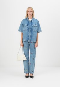 Jachetă din denim cu mâneci scurte, de culoare albastru deschis, cu două buzunare la piept; asociată cu pantaloni asortați care au motive brodate colorate. Geantă mică albă.