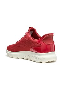 Scarpa sportiva rossa con parte superiore in rete e tallone lucido. Presenta un motivo di maglia testurizzato, suola bianca e colletto imbottito per il comfort.