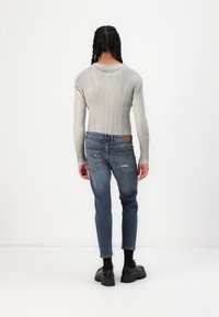 Sivý rebrovaný top s dlhým rukávom a tmavomodré úzke roztrhané džínsy. Model má na sebe čierne robustné topánky. Minimalistické pozadie.