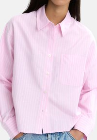 Jasnoróżowa koszula na guziki z cienkimi białymi pionowymi paskami, z długimi rękawami i kieszenią na piersi, wykonana z miękkiego materiału.