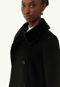 Black coat with a faux fur collar, featuring two buttons, a tailored fit, and a soft texture. Simple design with no visible patterns.