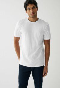 Camiseta de algodón blanca con mangas cortas, cuello redondo y un corte holgado, combinada con jeans de mezclilla azul oscuro. Textura suave y diseño minimalista.