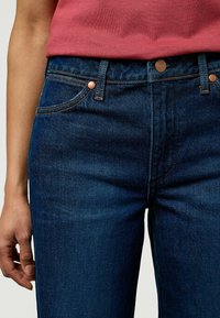Mørkeblå denimjeans med klassisk passform. Har kobbernitter, standard lommedesign og synlig søm. Glatt tekstur.
