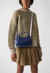 Blauwe leren handtas met een ronde bovenkant, zilveren hardware en een gedraaide handgreep. Draag met een gestreepte trui en een geplooide rok.