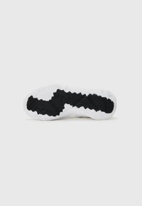 Sole of a sneaker featuring a white surface with textured black rubber tread patterns and an undulating design for grip and traction.