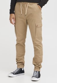 Kaki cargo bukser med elastiske manchetter, snørebånd i taljen og sidelommer. Stilet med sorte høje sneakers.