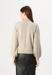 Ljust beige tröja med hög krage, ballongärmar och texturerad bak söm. Kombinerad med en åtsittande svart läderkjol.