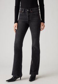 Jean droit à lavage foncé avec taille haute, braguette à boutons et design à cinq poches. Le tissu présente une texture usée et un effet de décoloration subtil.