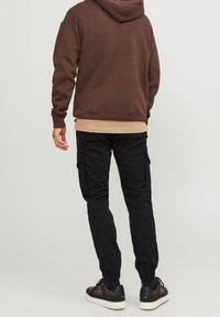 Hnědá mikina s volným střihem, kombinovaná s černými cargo kalhotami s bočními kapsami. Černé tenisky dotvářejí celý outfit.