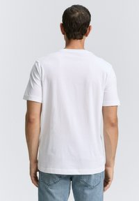 Camiseta de algodón blanca con mangas cortas y cuello redondo, con una textura suave y un corte relajado, vista desde la espalda.