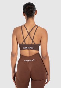 Ruskea urheiluliivi ja korkeavyötäröiset legginsit, joissa on SMILODOX-logo. Ominaisuuksiin kuuluvat ristikkäiset olkaimet ja uurrettu pinta, tiukka muotoilu, saumatön viimeistely.