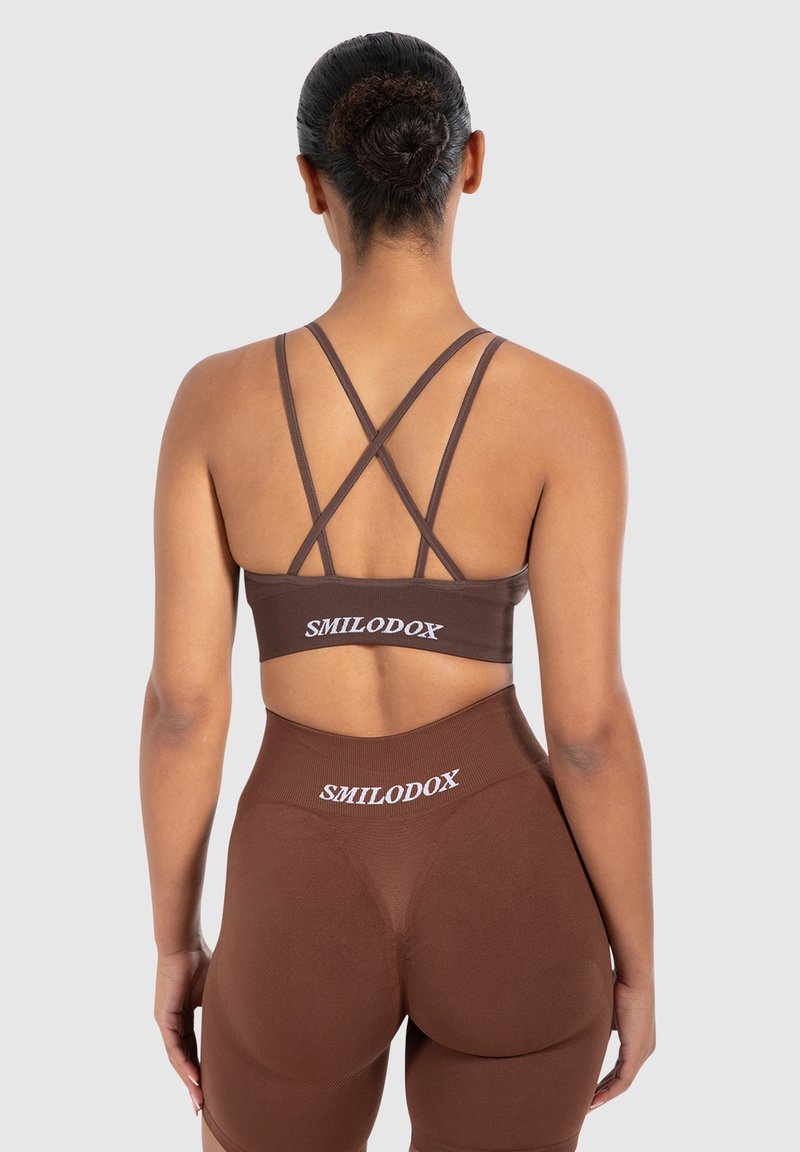 Ruskea urheiluliivi ja korkeavyötäröiset legginsit, joissa on SMILODOX-logo. Ominaisuuksiin kuuluvat ristikkäiset olkaimet ja uurrettu pinta, tiukka muotoilu, saumatön viimeistely.