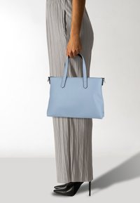 Borsa tote in pelle azzurro cielo con due manici corti, texture liscia e design minimalista. Le finiture includono bordi delle cerniere neri e cuciture.