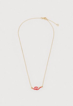 Złoty naszyjnik z łańcuszkiem, ozdobiony czerwonym, sercowatym wisiorkiem o zakrzywionym kształcie, zaakcentowany dwoma małymi złotymi koralikami.