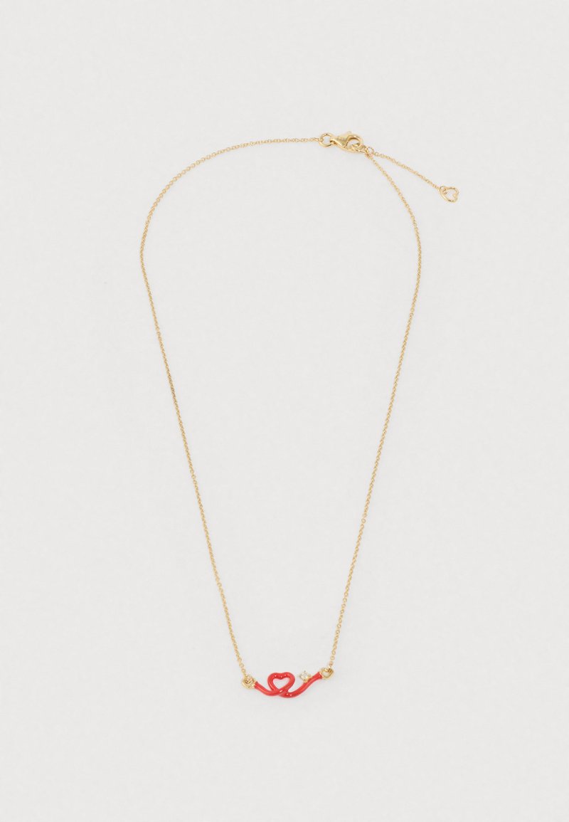 Zlatý reťazový náhrdelník so červeným príveskom v tvare srdca s prehnutým dizajnom, zvýraznený dvoma malými zlatými korálkami.