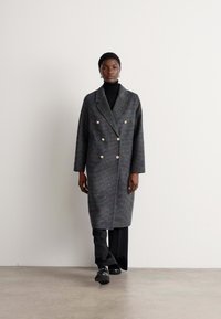 Grijs wollen mix double-breasted jas met grote knopen, met reverskraag en lange mouwen, gecombineerd met een zwarte turtleneck en broek.