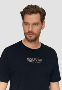 Dunkelblaues Baumwoll-T-Shirt mit kurzen Ärmeln und Rundhalsausschnitt. Das vordere Design zeigt in weißen Stickereien "S.O.LIVER CASUAL APPAREL".