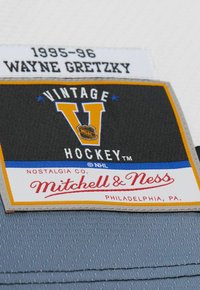 Patch vintage NHL con sfondo nero e accenti arancioni e gialli, che presenta le scritte "VINTAGE," "HOCKEY™" e "Mitchell & Ness."