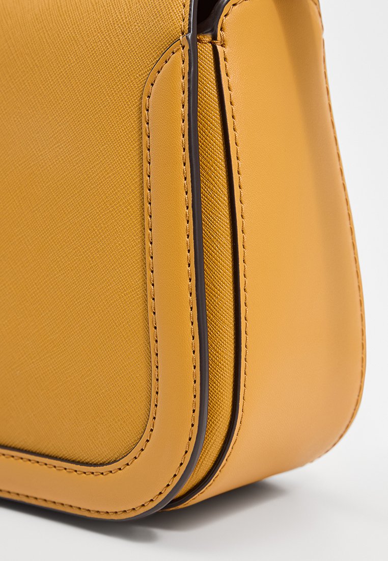 Nahaufnahme einer senfgelben Lederhandtasche mit glatten und strukturierten Elementen sowie detaillierter Naht auf weißem Hintergrund.