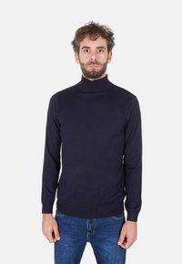 Maglione dolcevita blu navy realizzato in morbido tessuto a maglia, con una vestibilità aderente e polsini e orlo a coste, abbinato a jeans blu.